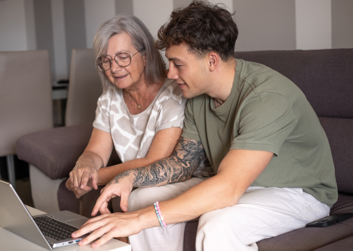 Ung mand hjælper lidt ældre kvinde med noget på en pc mens de sidder i sofaen