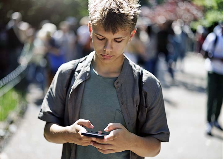 Teenagedreng der går rundt udenfor og kigger ned på sin mobiltelefon
